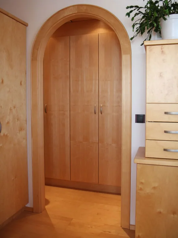 Eingebauter Schrank aus hellem Holz mit Rundbogen, daneben ein Kästchen mit Laden